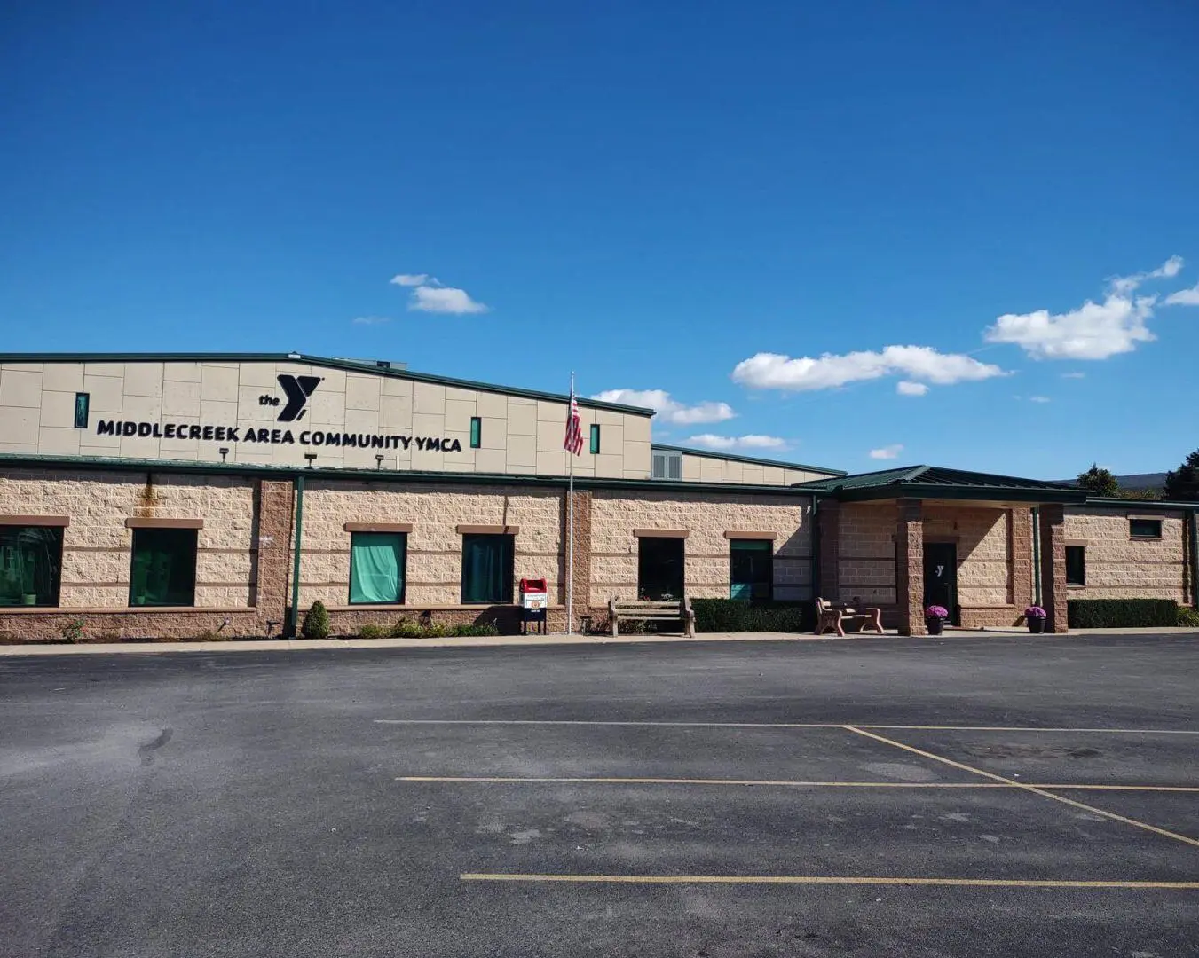 A photo of the Middle Creek Area Community Center. A tan building with a green roof and a parking lot out front.